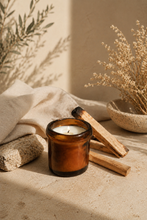 Load image into Gallery viewer, Handpoured Palo Santo beeswax candle in amber glass jar beside real Palo Santo wood sticks — made with pure rare Palo Santo essential oil for authentic meditation and stress relief